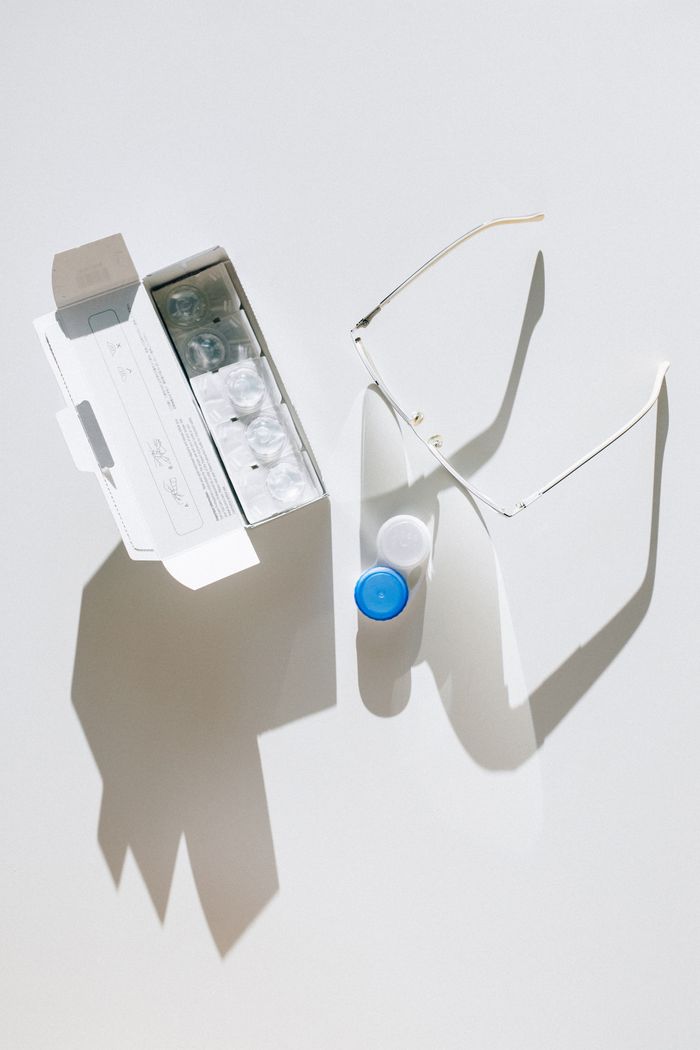 Top view of contact lenses, glasses, and a lens case on a white background.