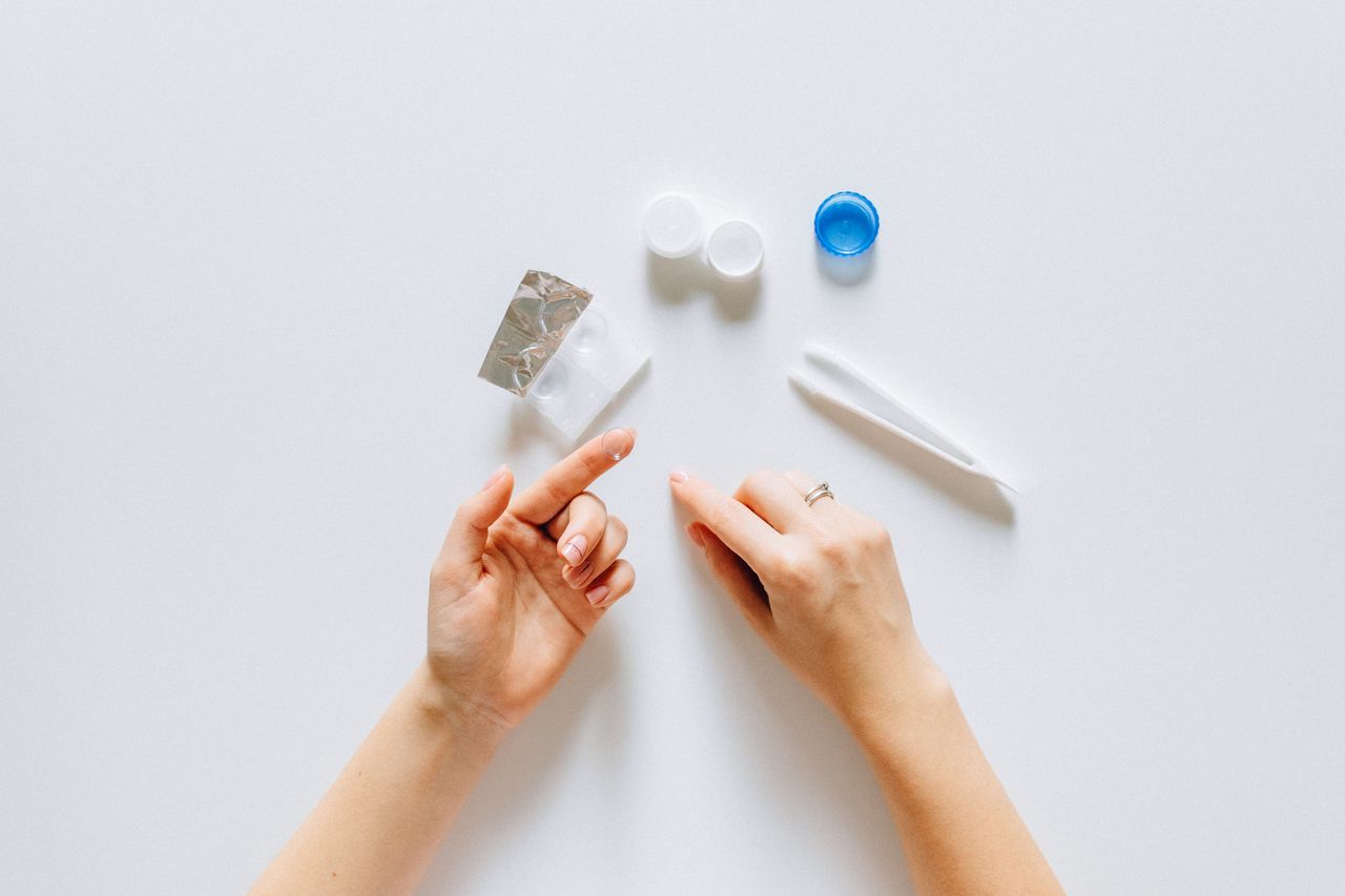 Hands arranging contact lens accessories on white background, emphasizing vision care.