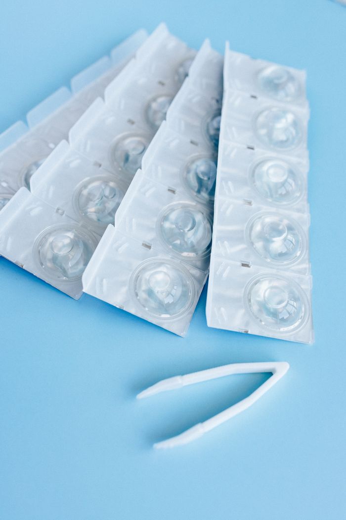 Disposable contact lenses arranged neatly with tweezers on a blue background.