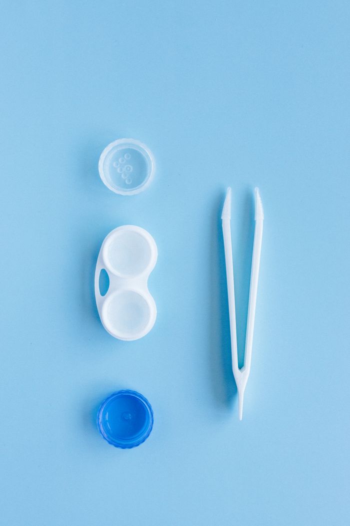 A contact lens kit featuring a lens case and tweezers arranged on a blue background in flat lay style.