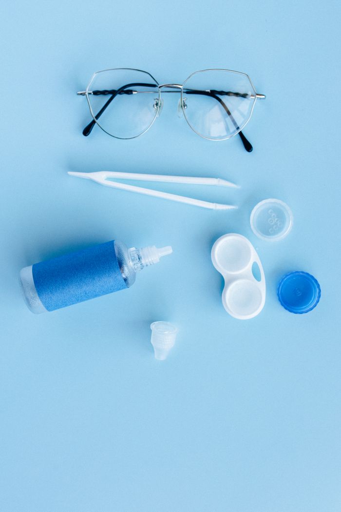 Flat lay of eye care essentials including glasses and contact lens solution on a blue background.